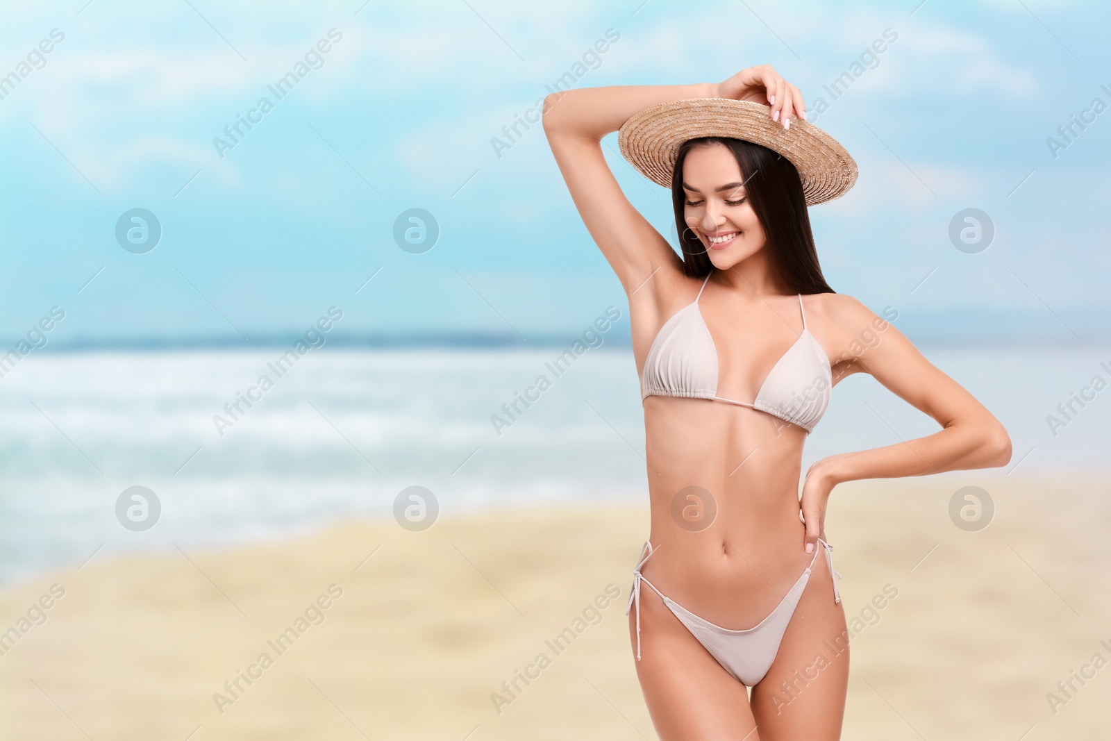 Image of Happy woman in stylish bikini and hat on sandy beach near sea, space for text