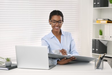 African American intern with folder working at white table in office