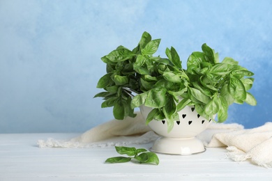 Colander with basil leaves on table against color background. Space for text