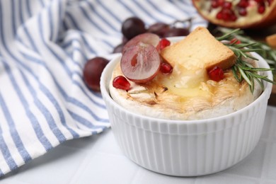 Photo of Tasty baked camembert with crouton, grape and rosemary on white tiled table, closeup. Space for text