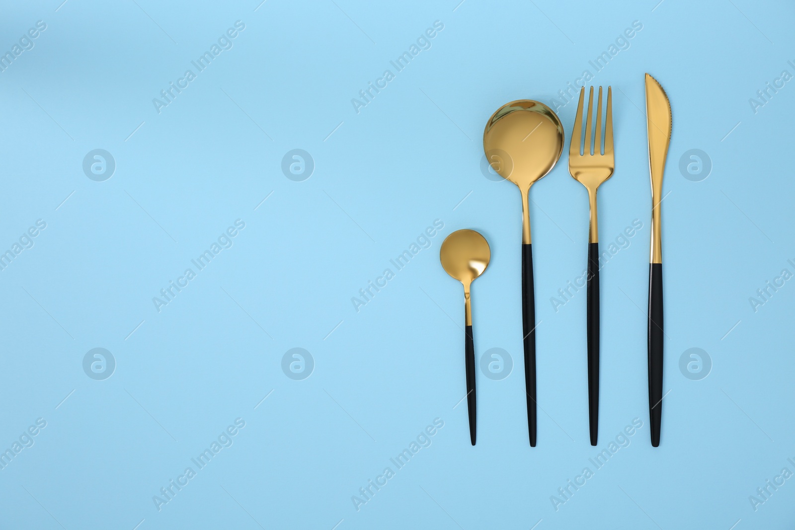Photo of Stylish golden cutlery set on light blue background, flat lay. Space for text