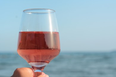 Photo of Woman holding glass of tasty rose wine near sea, closeup. Space for text