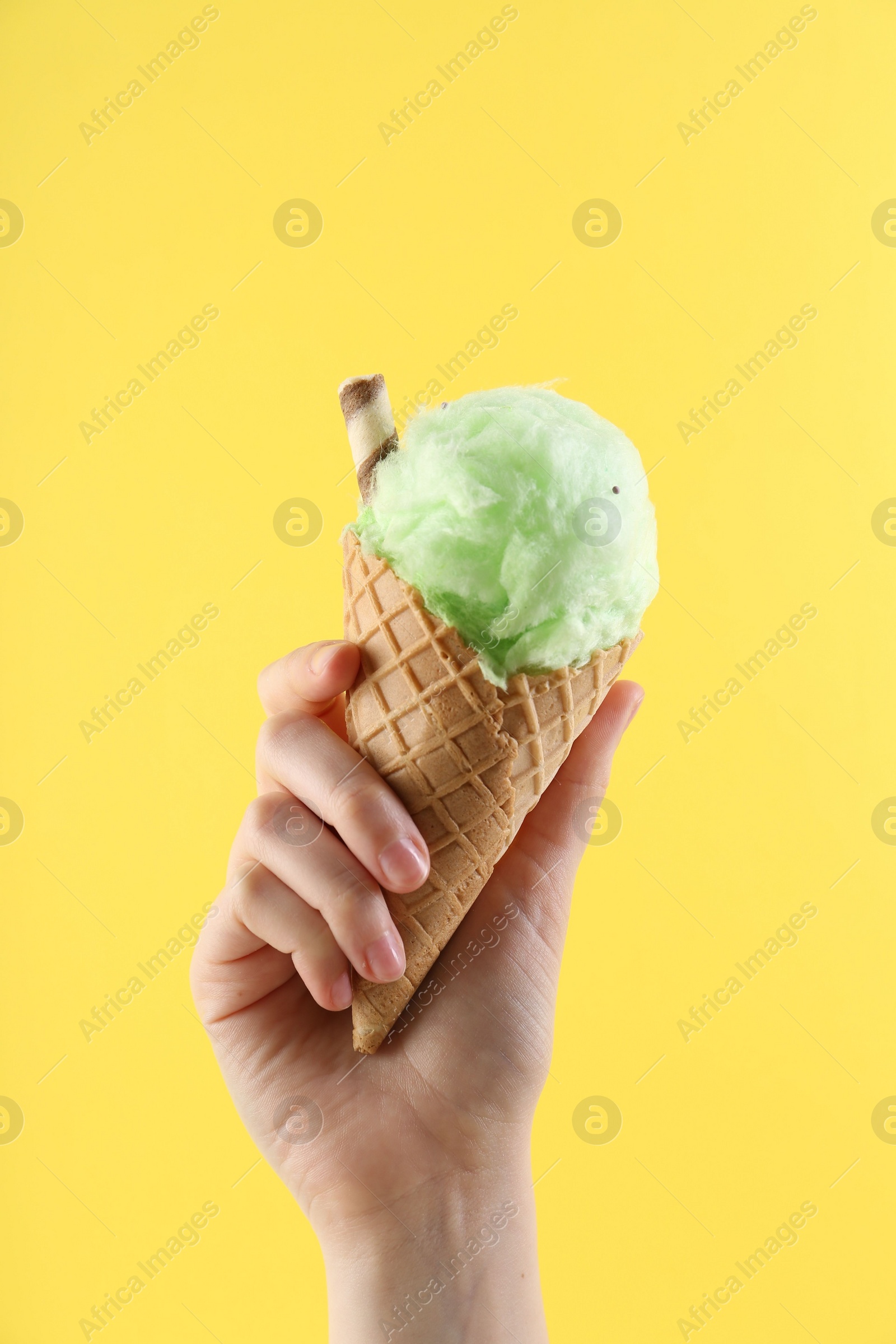 Photo of Woman holding waffle cone with cotton candy on yellow background, closeup