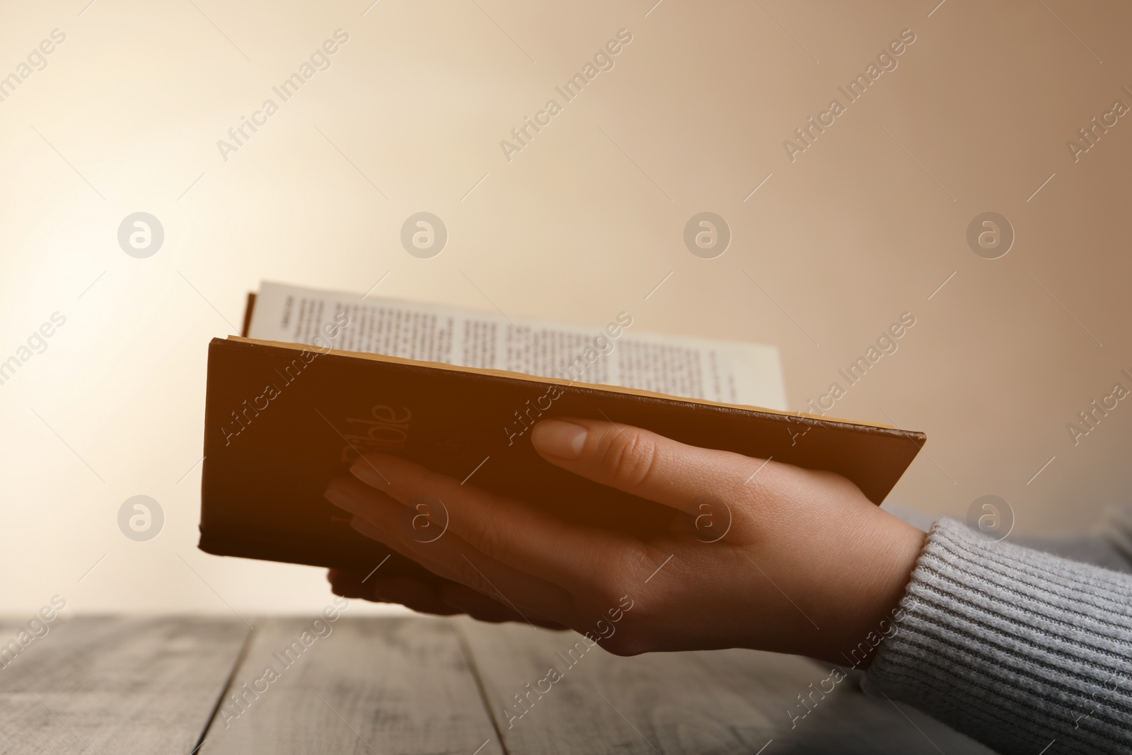 Photo of Woman reading Bible at wooden table, closeup