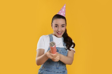 Photo of Young woman blowing up party popper on yellow background
