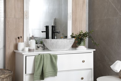 Photo of Chest of drawers with vessel sink, toiletries and houseplants in bathroom. Interior design