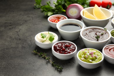 Photo of Different tasty sauces in bowls and ingredients on grey table, space for text