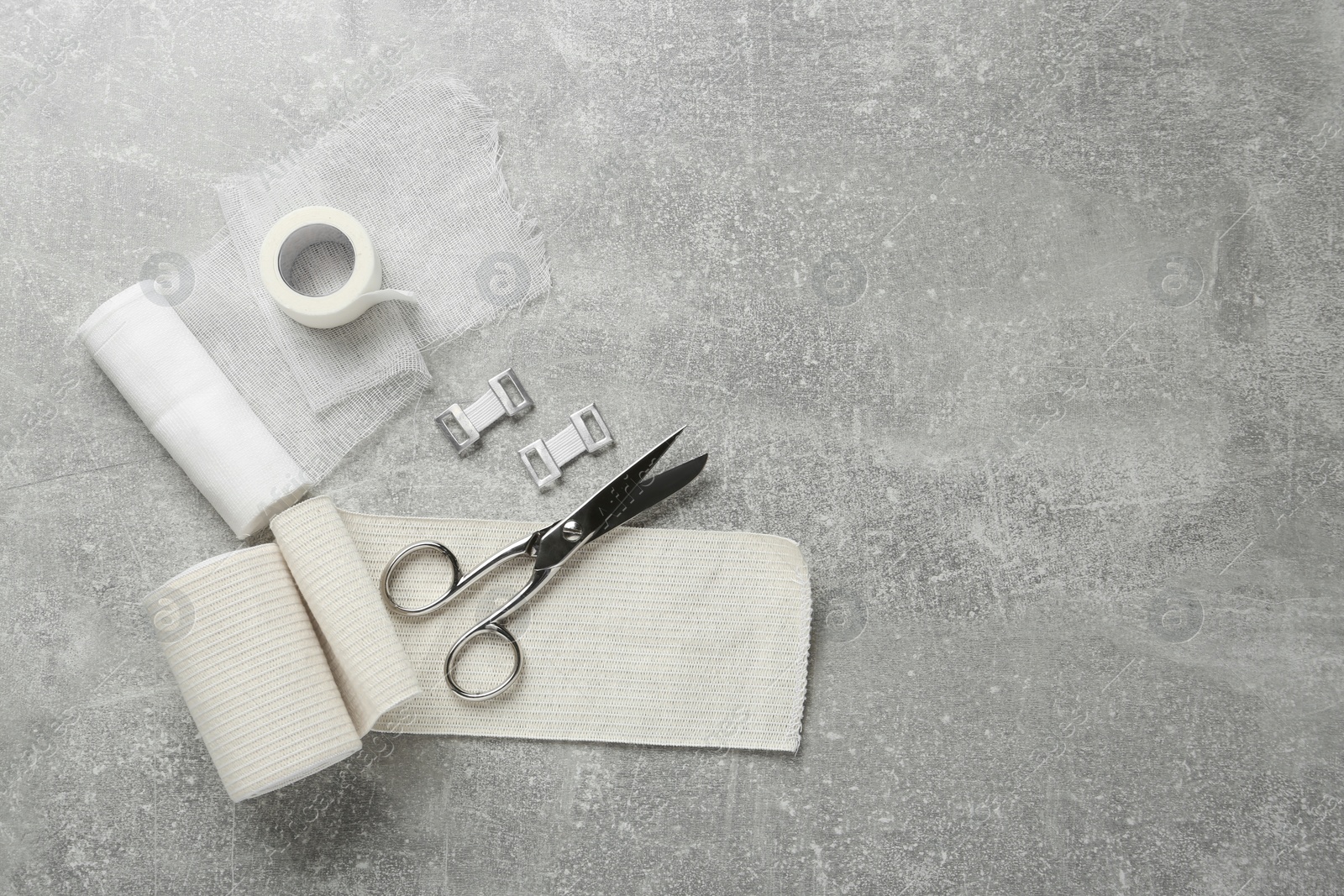 Photo of Medical bandage rolls, sticking plaster and scissors on grey table, flat lay. Space for text