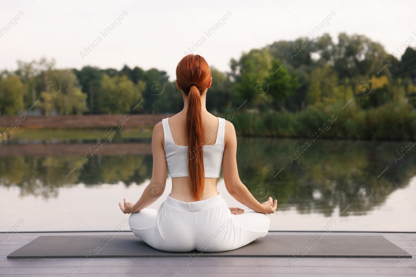 Photo of Woman practicing Padmasana on yoga mat outdoors, back view. Lotus pose