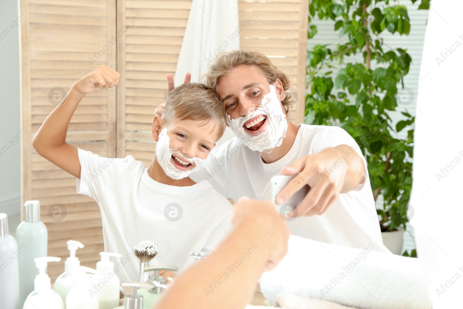 Photo of Father and son taking selfie with shaving foam on faces in bathroom