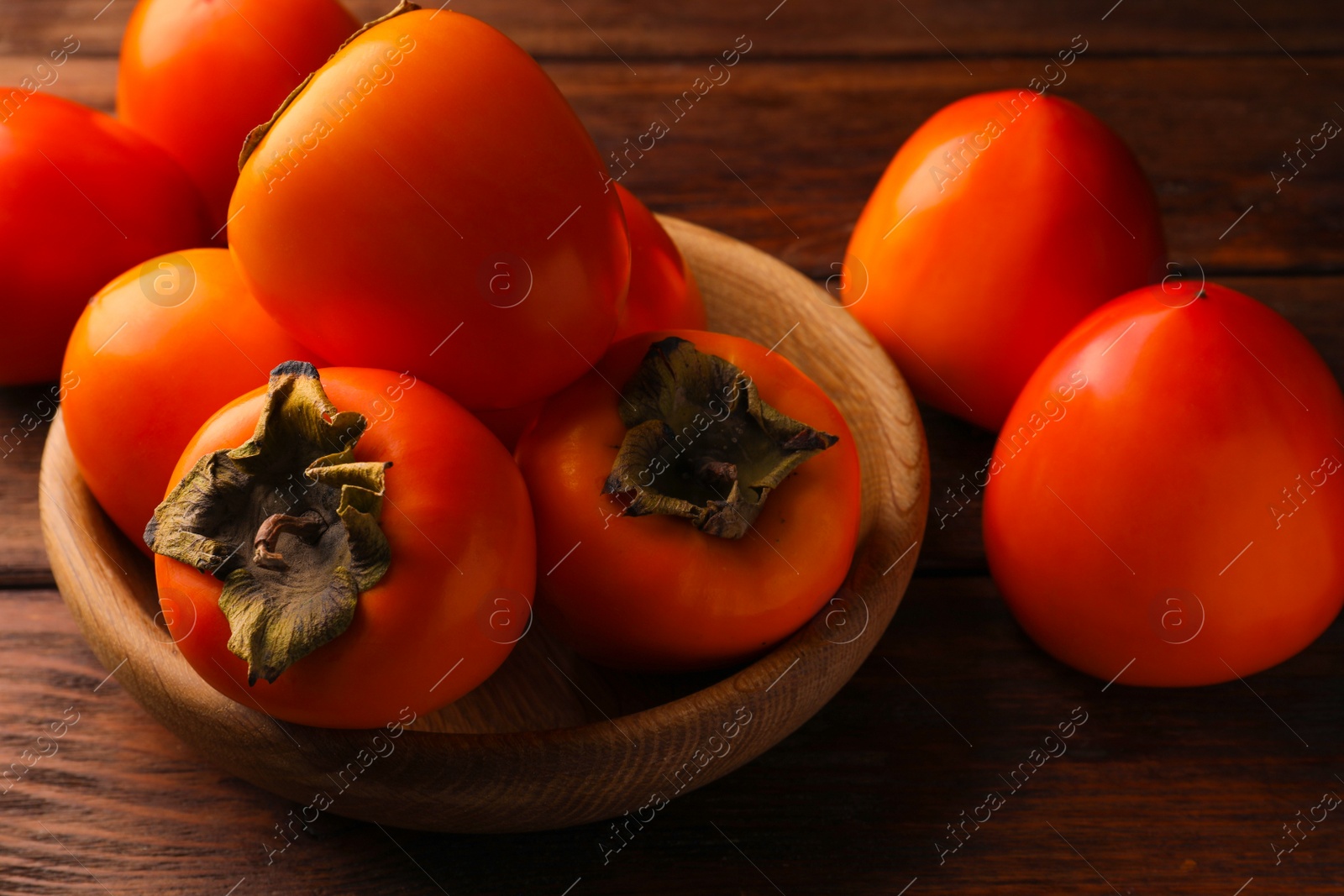 Photo of Delicious ripe persimmons in bowl on wooden table, closeup