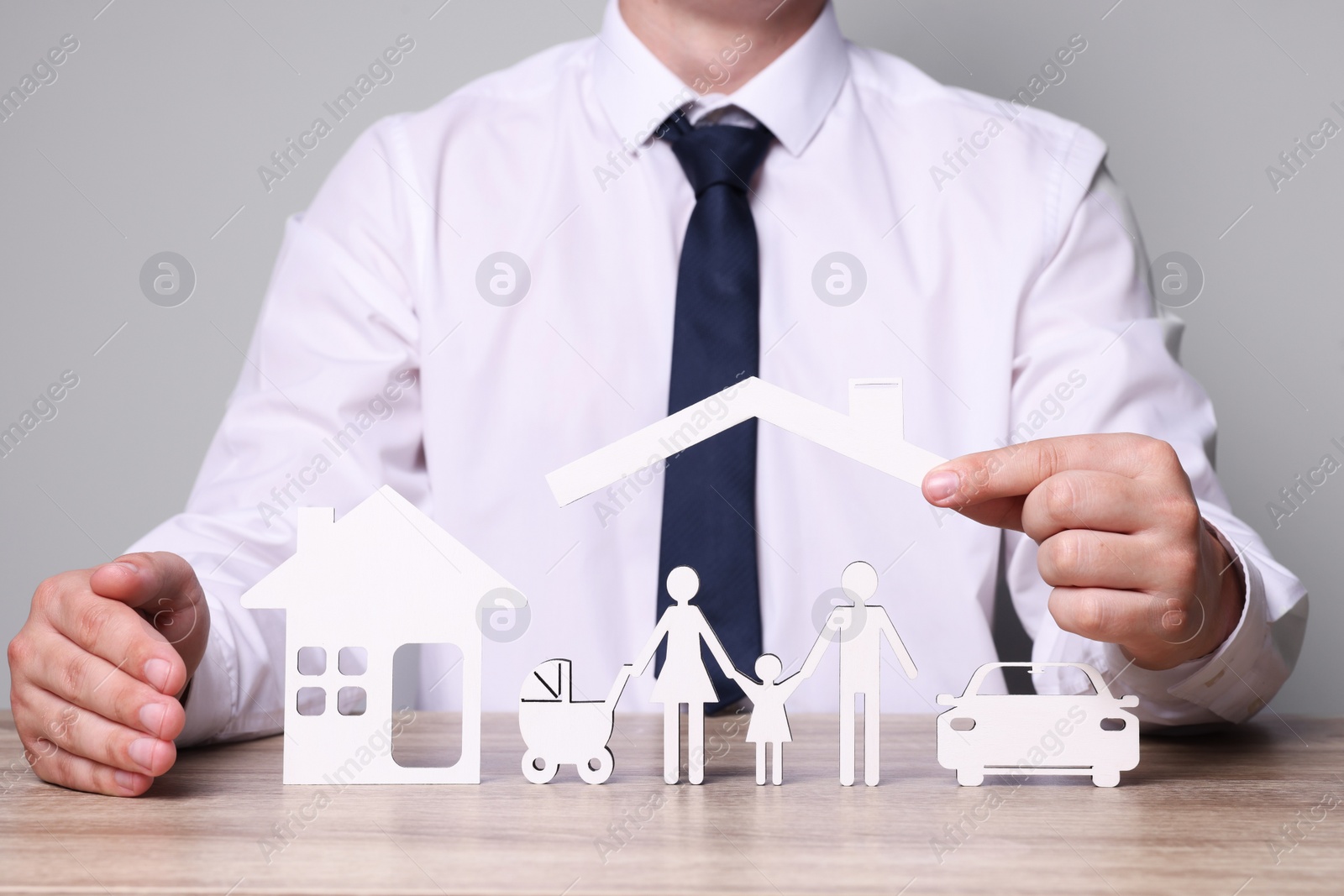 Photo of Man protecting figures of family, car and house at wooden table. closeup. Insurance concept