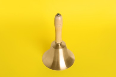 Photo of Golden school bell with wooden handle on yellow background