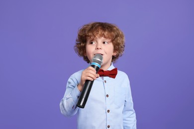 Photo of Cute little boy with microphone singing on violet background