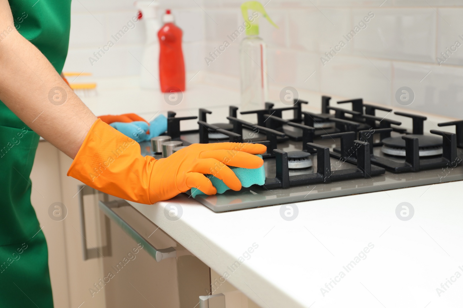 Photo of Woman cleaning gas stove with sponge in kitchen