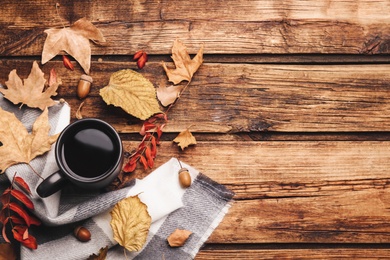 Photo of Flat lay composition with cup of hot drink and autumn leaves on wooden table, space for text. Cozy atmosphere