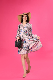 Photo of Young woman wearing floral print dress and straw hat on pink background