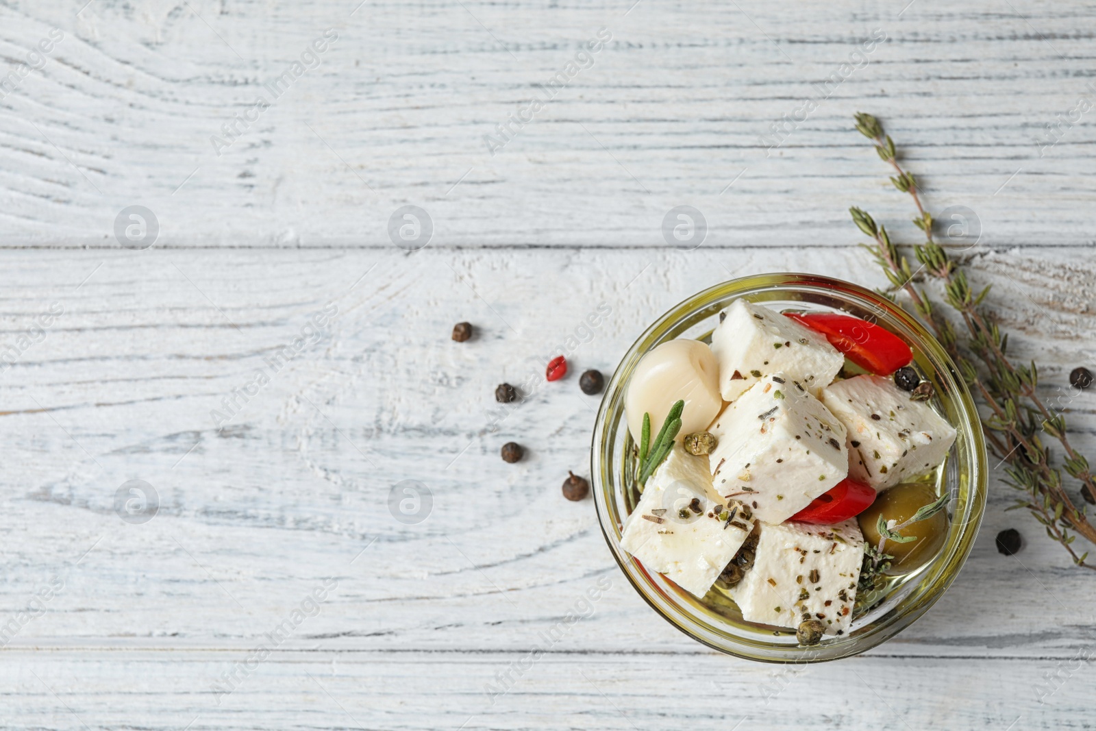 Photo of Pickled feta cheese in bowl on white wooden table, top view. Space for text