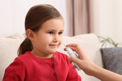 Mother using nasal spray to treat her little daughter on sofa indoors, closeup