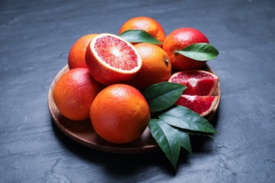 Photo of Plate of ripe red oranges and green leaves on dark table
