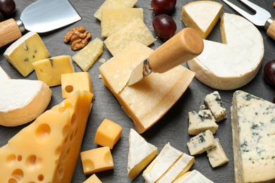 Photo of Cheese platter with specialized cutlery on black table, closeup view