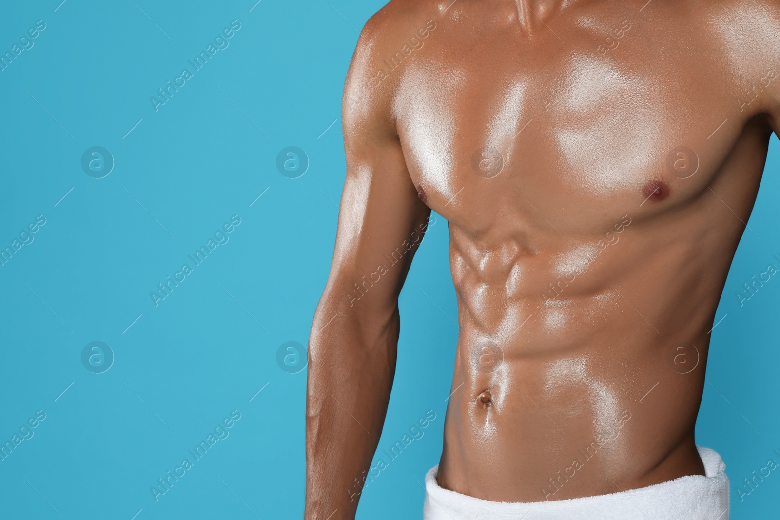 Photo of Shirtless man with slim body and towel wrapped around his hips on light blue background, closeup