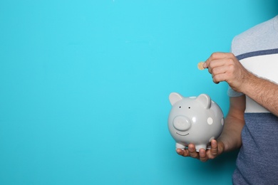 Photo of Man putting coin into piggy bank on color background, closeup with space for text