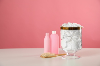 Jar with cotton pads on white table against pink background. Space for text