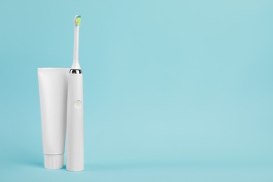 Photo of Electric toothbrush and toothpaste on light blue background, space for text