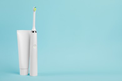 Electric toothbrush and toothpaste on light blue background, space for text