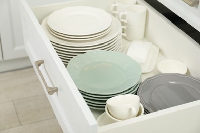 Photo of Clean plates, cups and bowl in drawer indoors