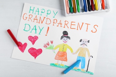 Photo of Beautiful drawing with phrase Happy Grandparents Day on white wooden table, flat lay