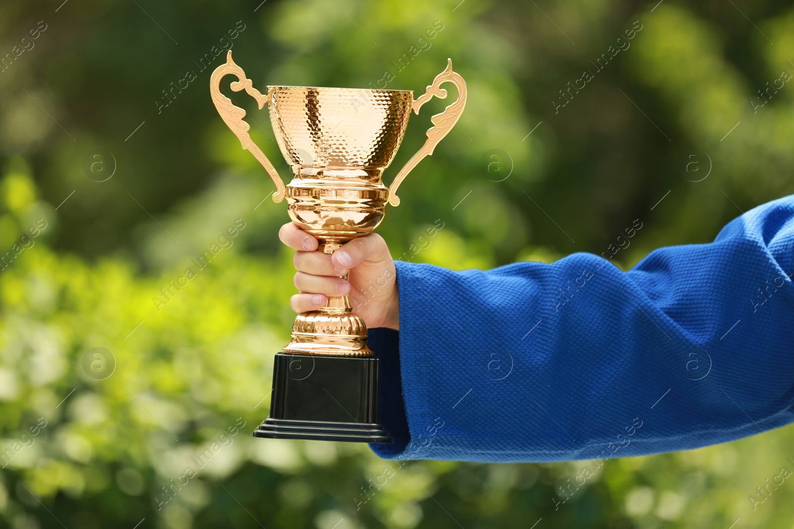 Photo of Young man in blue kimono with gold trophy cup outdoors, closeup