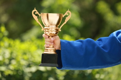 Photo of Young man in blue kimono with gold trophy cup outdoors, closeup