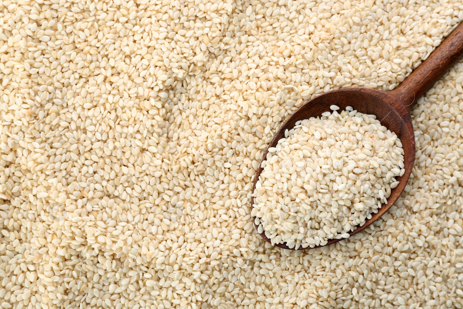 Photo of Wooden spoon on pile of white sesame seeds, top view. Space for text