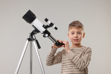 Cute little boy with telescope on light grey background