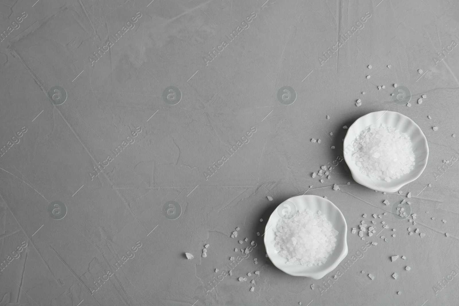 Photo of Plates with natural sea salt on grey table, flat lay. Space for text