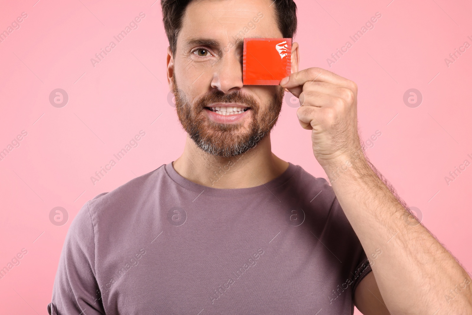 Photo of Man holding condom on pink background. Safe sex