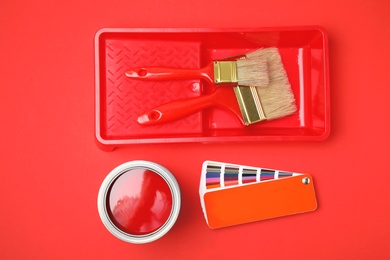 Flat lay composition with can of paint, brush and renovation tools on red background