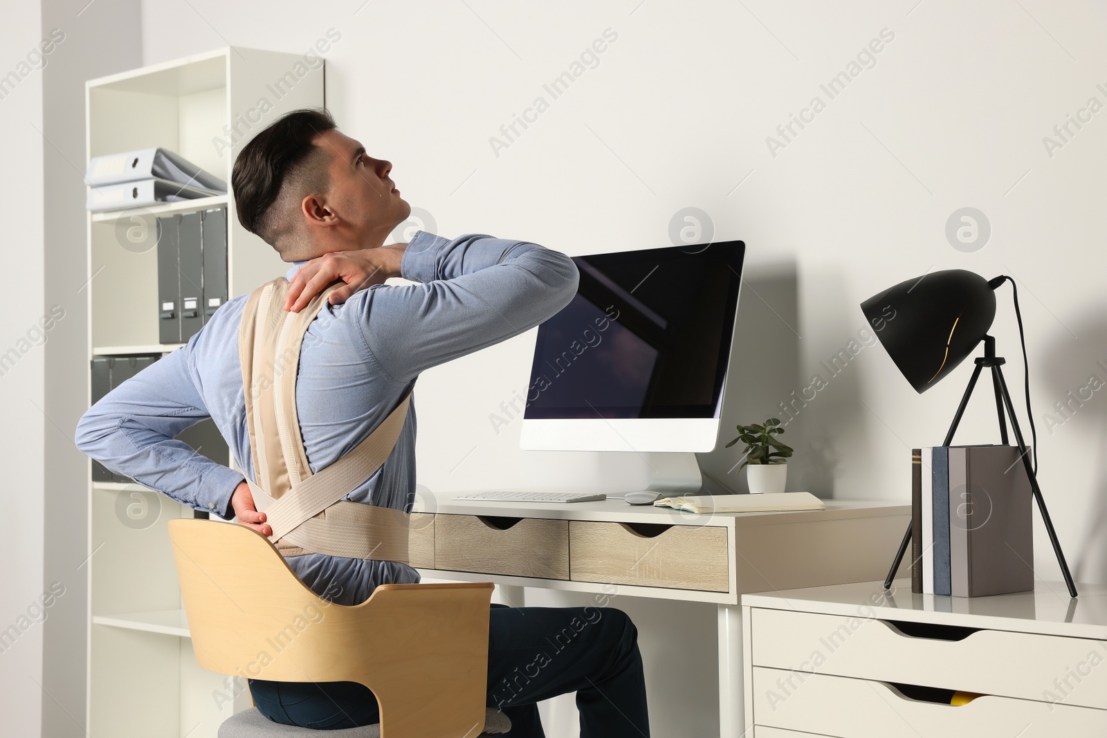 Photo of Man with orthopedic corset working on computer in room