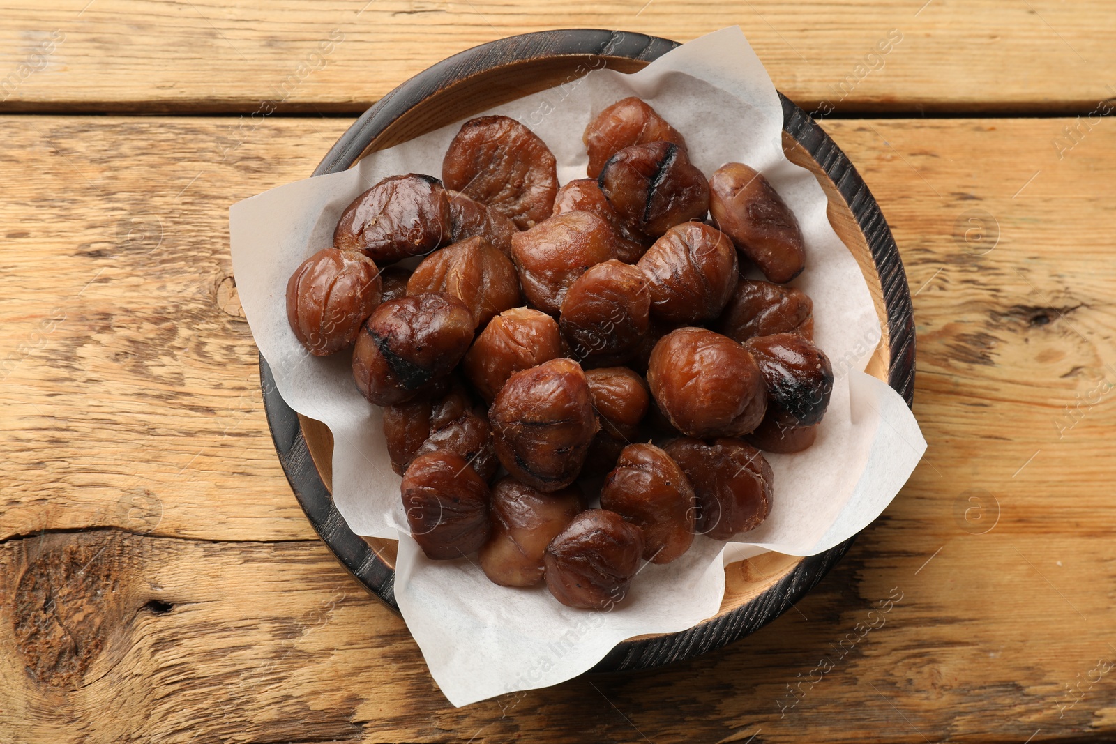 Photo of Roasted edible sweet chestnuts in bowl on wooden table, top view