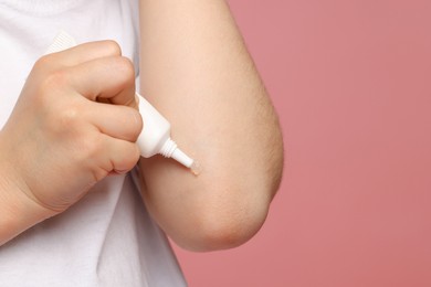 Child applying ointment onto elbow against pink background, closeup. Space for text