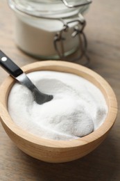 Photo of Baking soda in bowl on wooden table, closeup