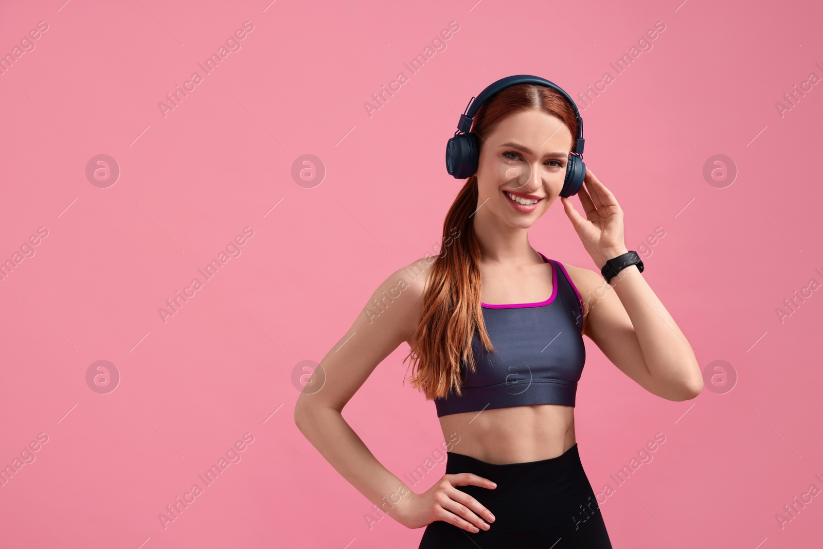 Photo of Woman in sportswear and headphones on pink background, space for text