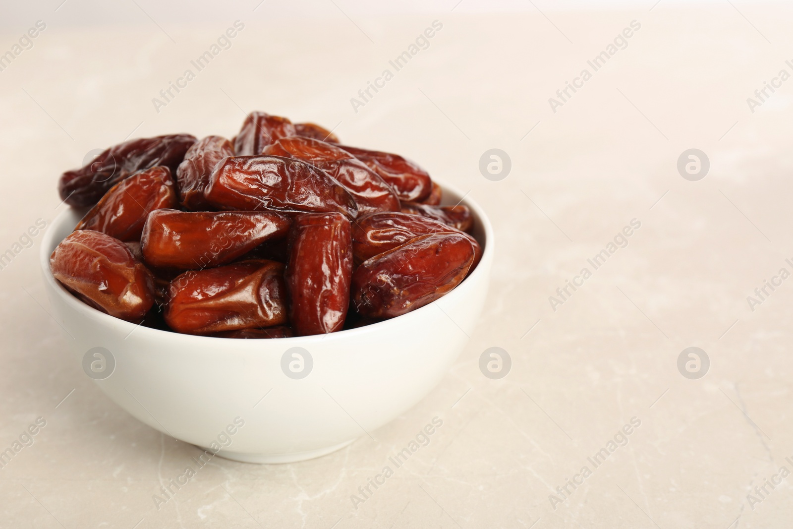 Photo of Sweet dried dates in bowl on light table. Space for text