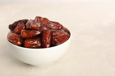 Photo of Sweet dried dates in bowl on light table. Space for text