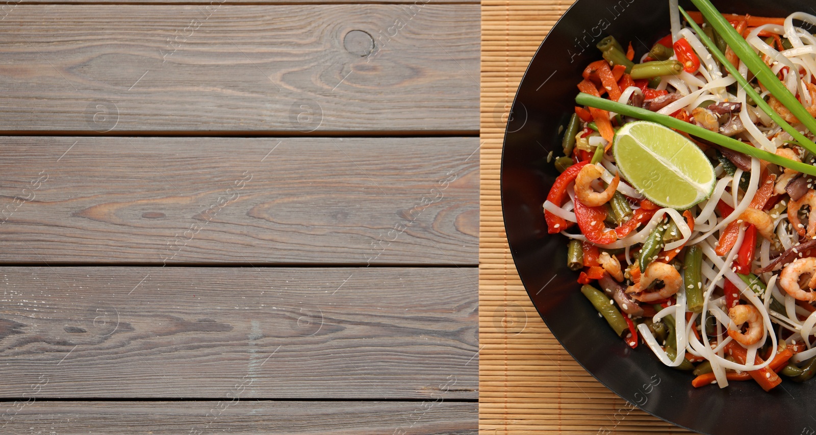 Photo of Shrimp stir fry with noodles and vegetables in wok on wooden table, top view. Space for text