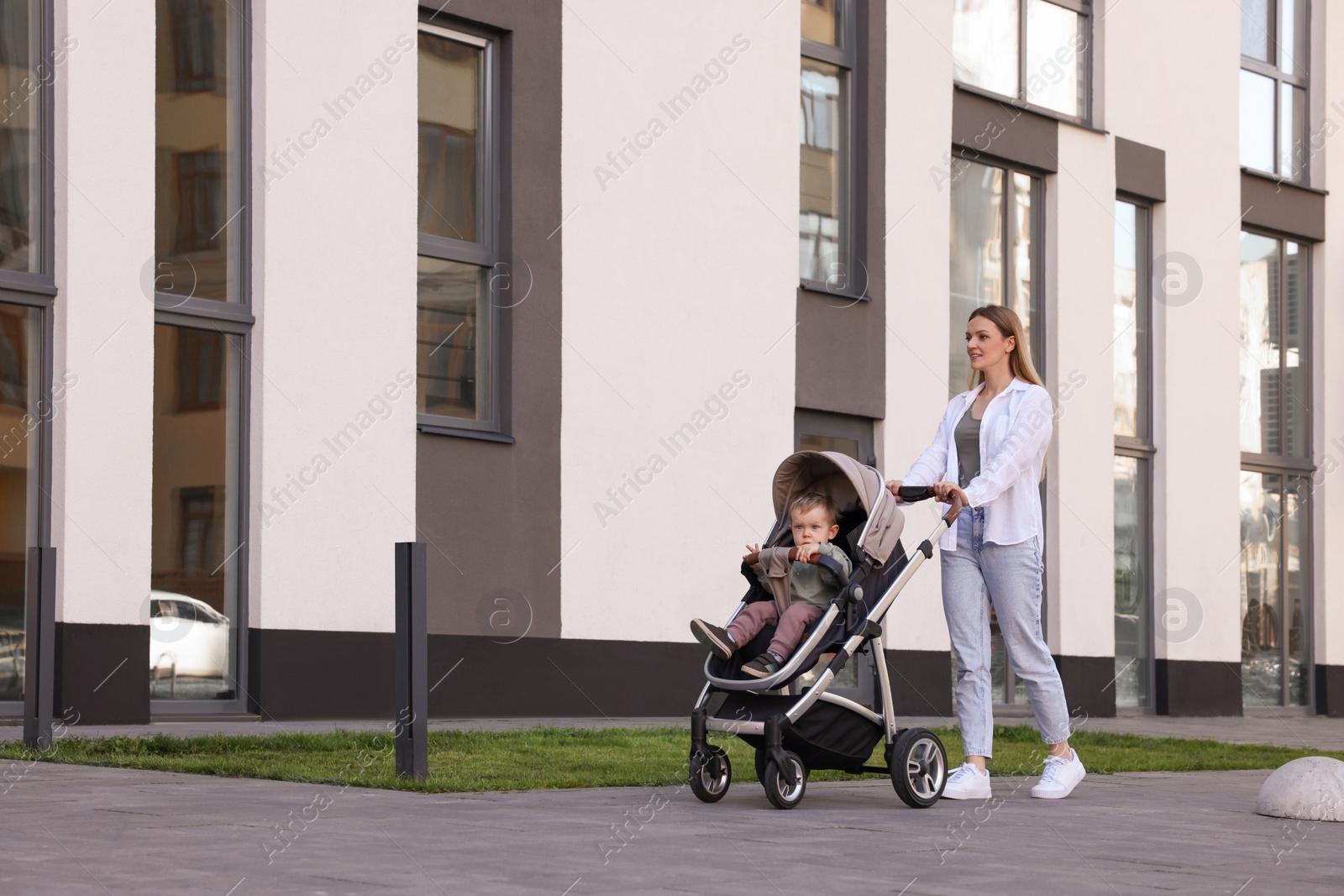 Photo of Beautiful nanny with cute little boy in stroller walking outdoors