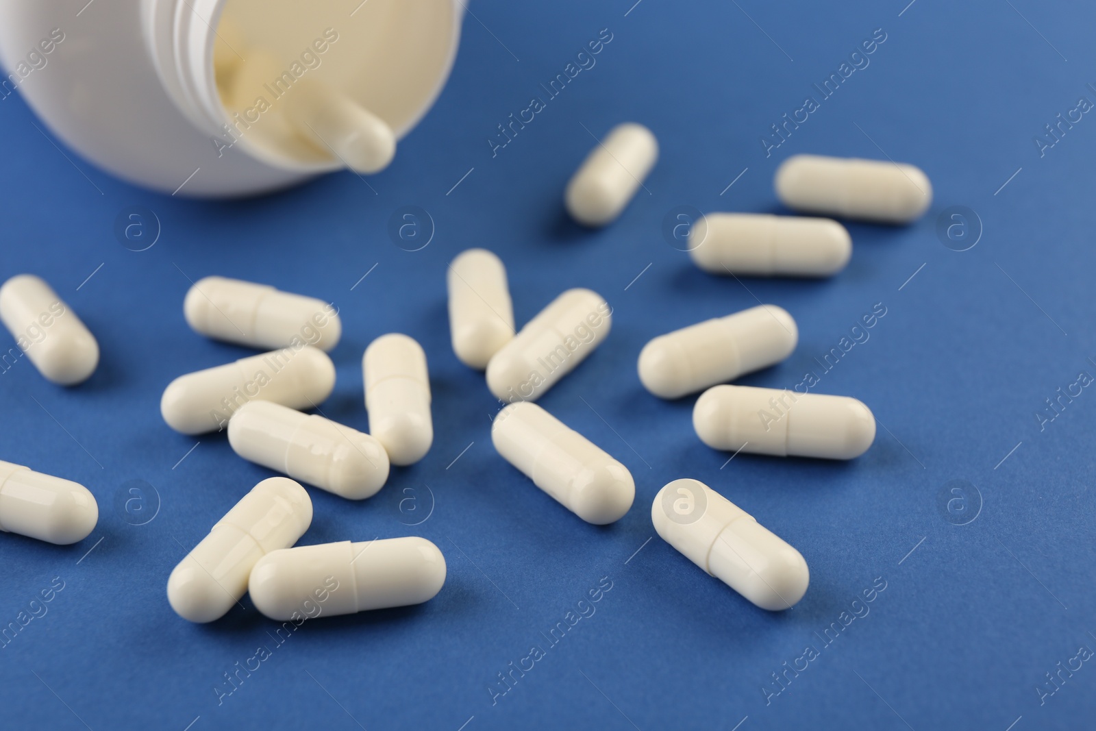 Photo of Bottle and vitamin capsules on blue background, closeup