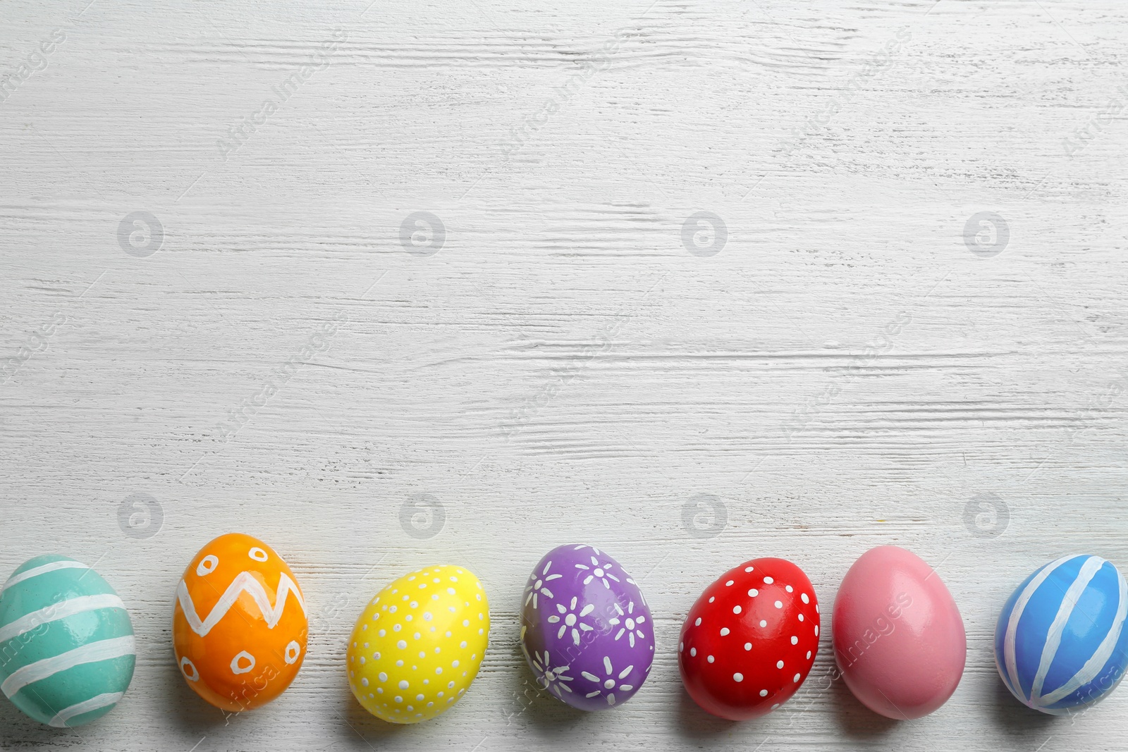 Photo of Flat lay composition of painted Easter eggs on wooden table, space for text